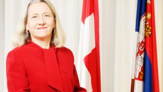 Alumna standing in front of the Swiss flag smiling at the camera.
