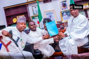 Three men sit together proudly holding up a document in a blue folder.