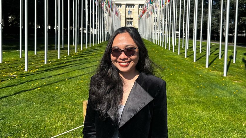 A woman standing with flags behind her on a sunny day in a field.