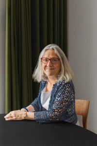 Alumna sat at a desk smiling at the camera.