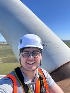 Santiago poses for a selfie while out in the field, wearing a helmet and high visibility jacket.
